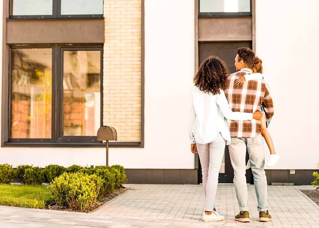 A woman and man together, holding their child as they look at their new house.